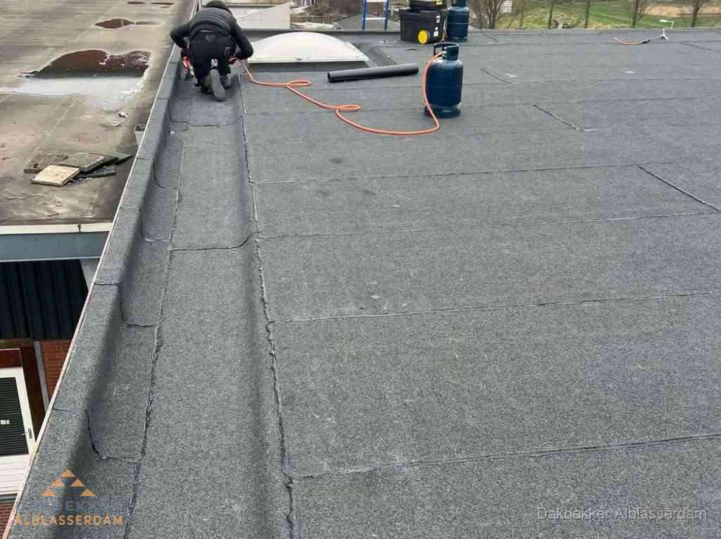 Dakdekker repareert bitumen dakbedekking op groot plat dak in Alblasserdam